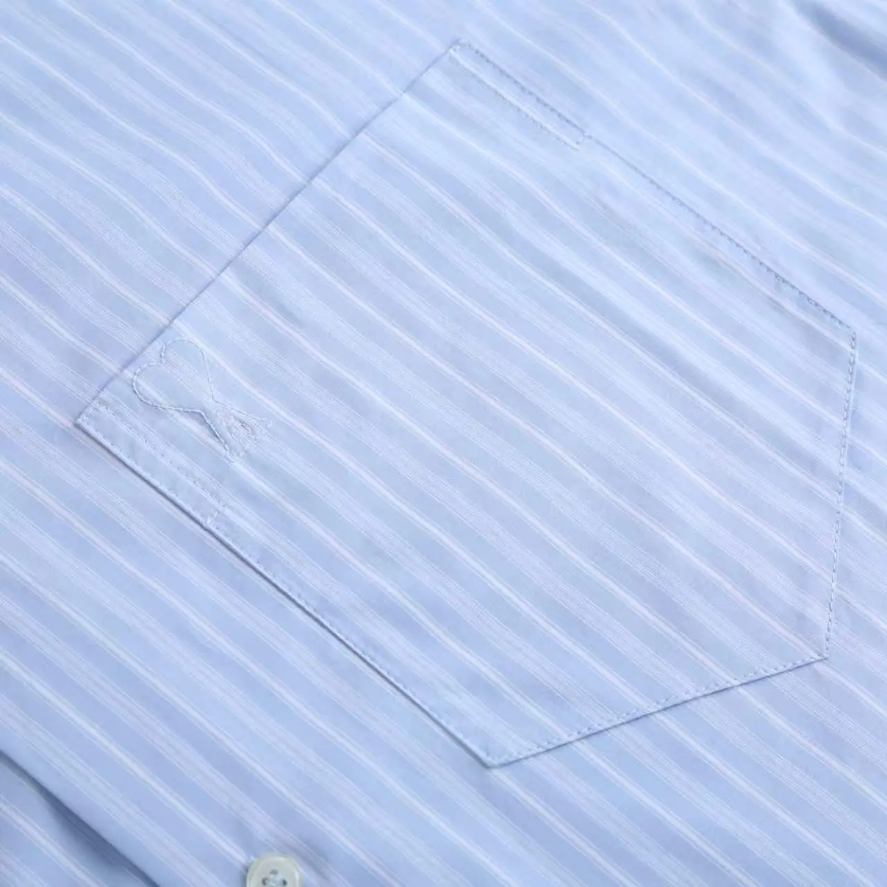 AMI Embroidered Striped Shirt Fabric Selection: Made of 100% cotton poplin fabric. The pure cotton fiber can quickly absorb moisture and perspire, making it refreshing and not stuffy when worn for a long time. The unique plain weave process of poplin makes the fabric both soft and skeletal, not easy to wrinkle and deform, and the upper body is neat and clean. Coupled with the fine blue and white stripes all over the body, the light color scheme is gentle and elegant, which can meet the needs of different scenes. Process 1: Accurately mark the embroidery position on the chest patch pocket to ensure that the pattern does not shift and does not destroy the overall beauty of the striped fabric. High-count embroidery threads of the same color as the fabric are selected, and flat stitch embroidery technology is used. The stitches are evenly tracked, the edges are clean and neat, and the love outline is simple and smooth. It retains recognition without irritating the skin. It is blended into the striped texture in a low-key manner to avoid an abrupt feeling, while ensuring that the embroidery threads are Wear-Resistant. 2: After the embroidery is completed, perform high-temperature ironing and thread trimming to ensure that the pattern is smooth and compliant, and it is not easy to lose thread or warp after being worn for a long time. Details: 1. The collar seat adopts double-layer reinforcement technology, which is not easy to collapse and deform after long-term wear. The collar corner has a soft arc, which can modify the neck line without being too sharp, making it neat and decent. 2. The inner side of the placket has hidden hemming treatment to avoid burrs on the fabric, while enhancing structural stability and preventing it from deforming after multiple washes. Accessories: One-to-one customized buttons Size: S M L XL Style number: D 236